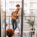 Mann umarmt Frau auf Balkon. Entspanntes Paar trinkt Kaffee am Wochenende.