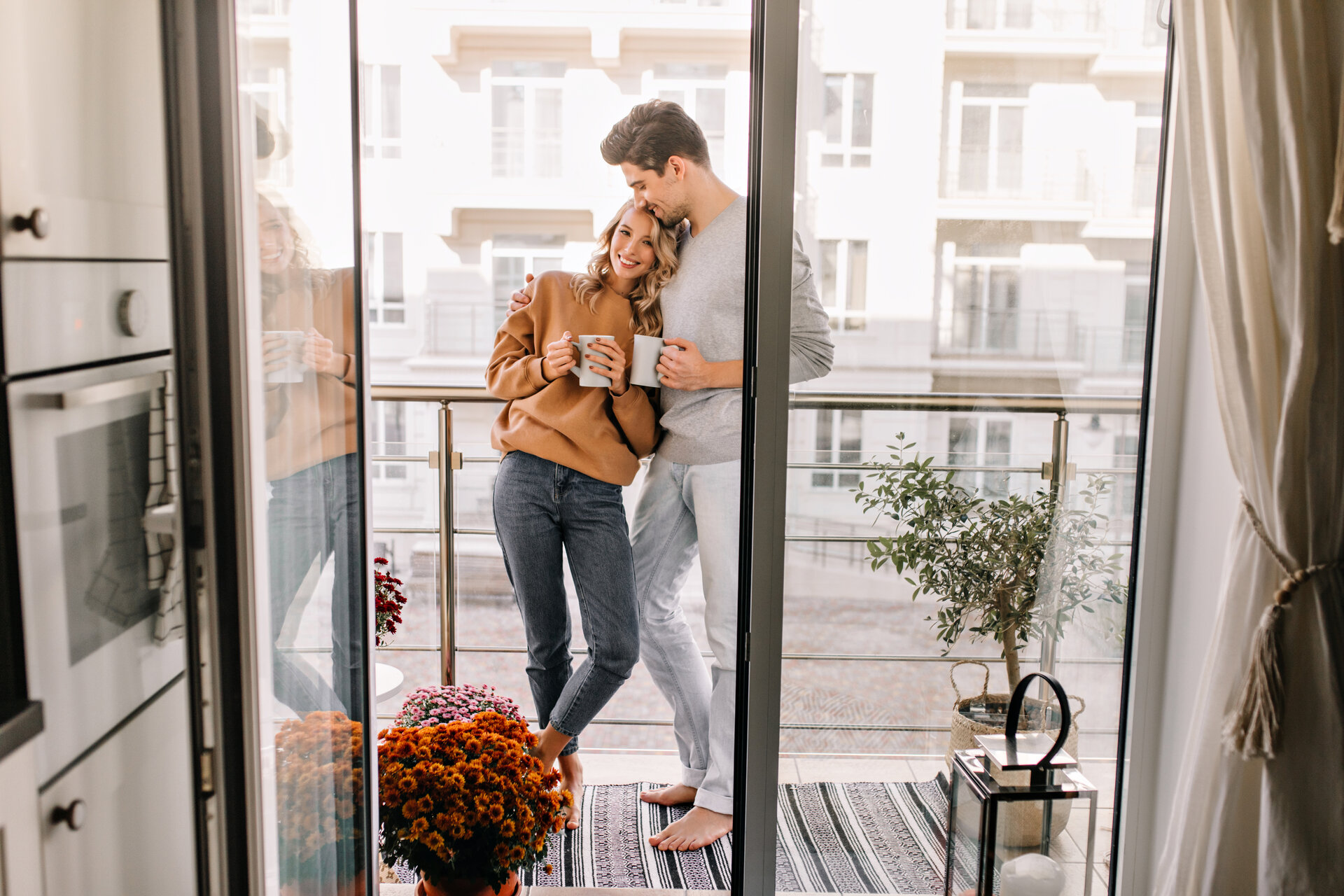 Mann umarmt Frau auf Balkon. Entspanntes Paar trinkt Kaffee am Wochenende.